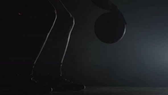 Silhouette of Basketball Player Dribbles Ball Practicing Skills in a Dark Studio with Smoke and