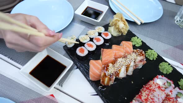 Female hand with chinese chopsticks takes sushi to dip in soy sauce