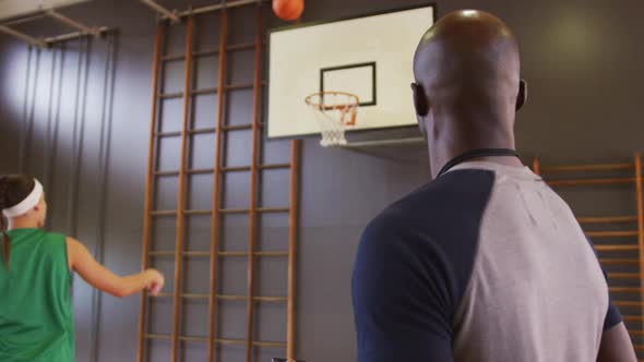 Diverse female basketball player and male coach practicing shooting with ball