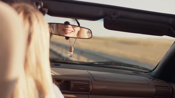 Girl Paints Her Lips While Looking in Rearview Mirror of Convertible