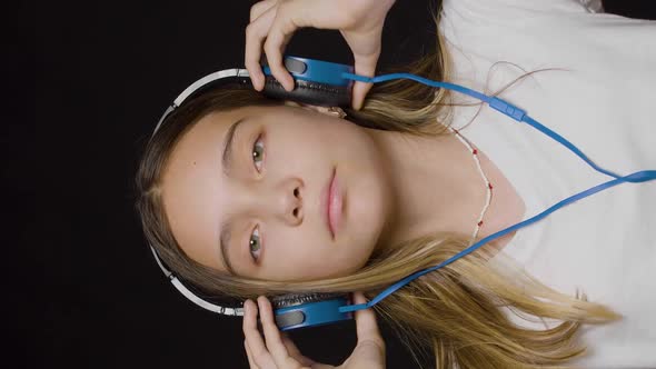 Teenage Girl Wearing Headphones and Listening to the Hard Rock Music on a Black Background