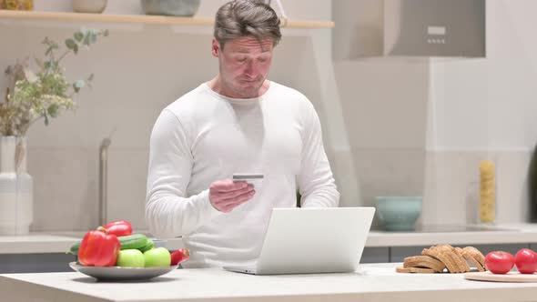 Middle Aged Man Making Online Payment on Laptop in Kitchen