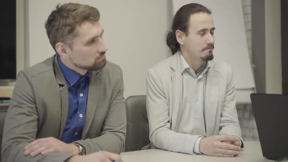 Camera Approaching Two Male Caucasian Office Workers Listening Attentively As Sitting at the Table