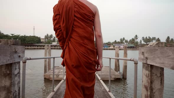 The monks are walking down to the waterfront using a wooden bridge. Slow motion. alt