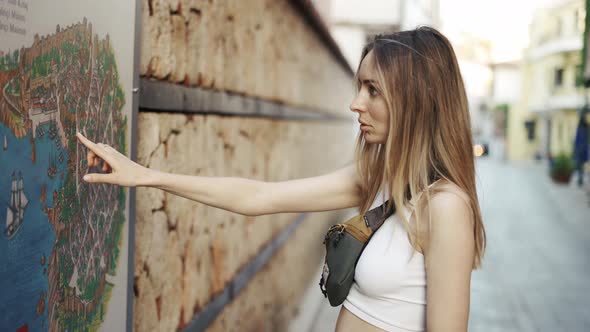 Blonde Female Tourist Standing By the Wall Map Pointing Finger