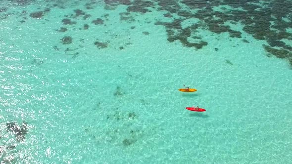 Aerial drone view of a man and woman couple kayaking around a tropical island.
