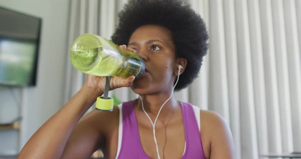 Happy african american wearing sportswear, using smartphone, drinking water