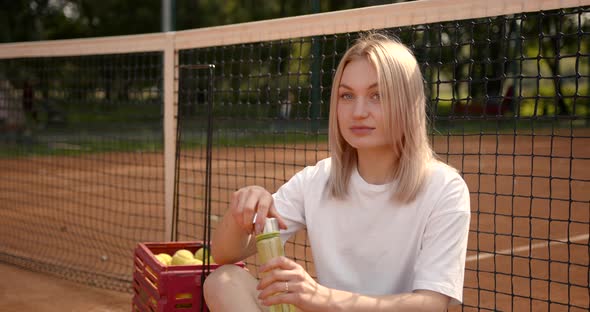 Woman Drinking Water Sitting on Tennis Court