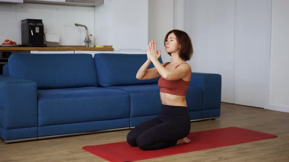 Relaxed Woman in Sportswear is Sitting on Yoga Mat Enjoying Meditation with Hands in Namaste