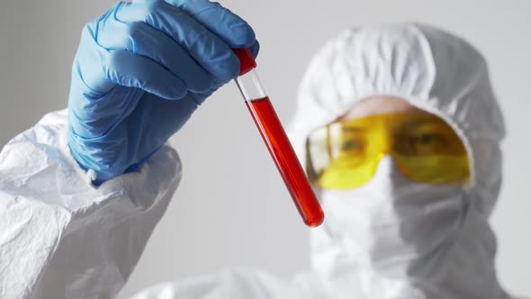 A Doctor in a White Protective Suit and Blue Disposable Gloves Examines a Blood Test of a Patient