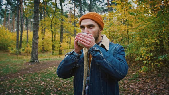 Male Tourist Warming Hands of Hot Tea Cup Drinking Beverage at Hiking Trip in Autumn Forest