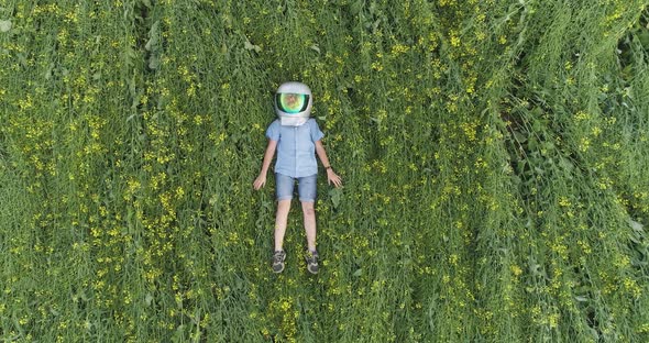 Dreamer Boy in an Astronaut Helmet Lies in a Field of Rapeseed and Dreams of Flying Into Space View