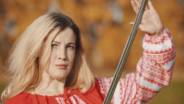 Feisty Woman in Red Clothes Standing on the Field and Posing with Sword