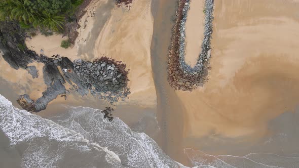 Aerial drone video looking down on a deserted tropical beach with a small creek flowing out to the o