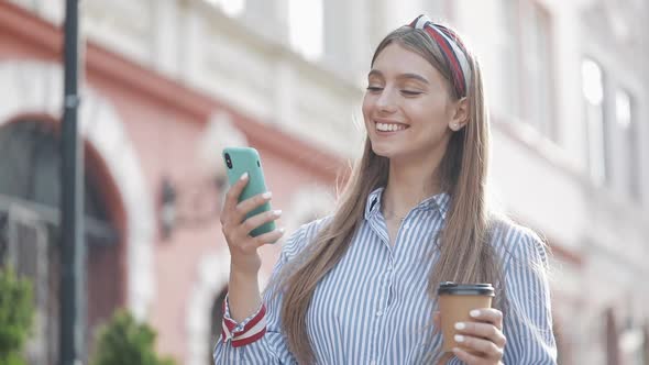 Portrait of Attractive Fashionable Young Caucasian Girl with Headband Using Her Smartphone and