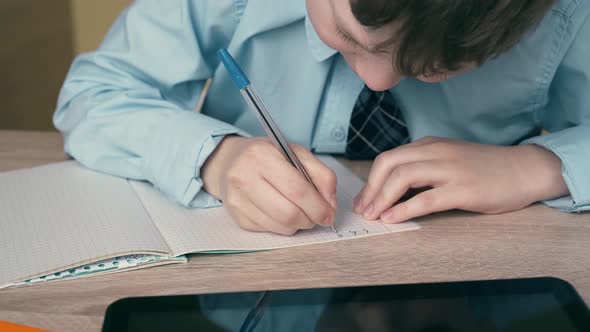 Ext CU, Tracking: Schoolboy Does Homework, Writes a Pen in a Notebook, on the Table Is a Tablet.