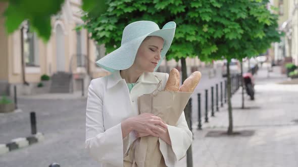 Middle Shot of Elegant Woman Tearing Piece of Baguette and Smiling at Camera. Portrait of Attractive