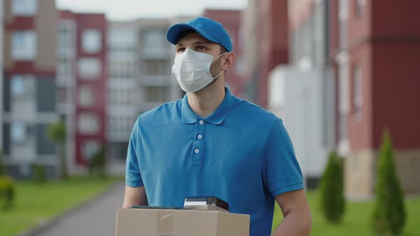 An Young Mailman Courier with a Protective Mask and Gloves is Delivering a Parcel Directly to a