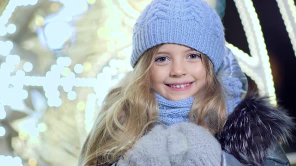 Portrait of Happy Cute Little Girl Looking at Camera on Blurred Christmas Lights Background