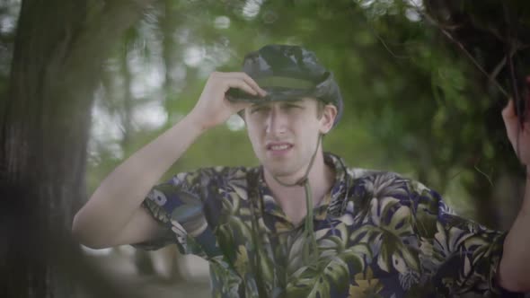 Young white man explores tropical jungle. Wearing Tilly hat and Hawaiian shirt. Scans the horizon wi