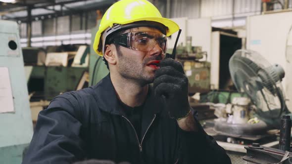 Factory Worker Talking on Portable Radio While Inspecting Machinery Parts