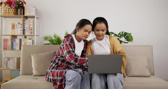 Twin girls planning for work to laptop while sitting on couch