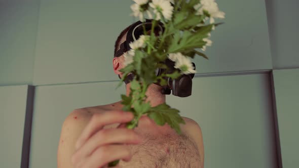 Faceless Shirtless Man in Gas Mask Smelling Flowers