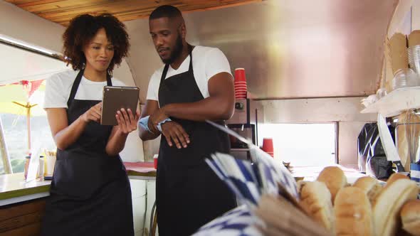 African american couple wearing aprons smiling while using digital tablet in the food truck