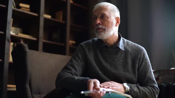 Close-up Portrait of Elderly Gray-haired Man Talking with Person in Dark Cozy Room