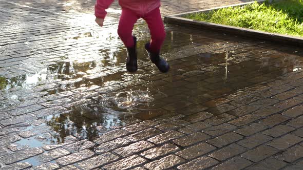 Slow Motion Blonde Child in Pink Jumps on Puddles Splashes Scatter From Boots