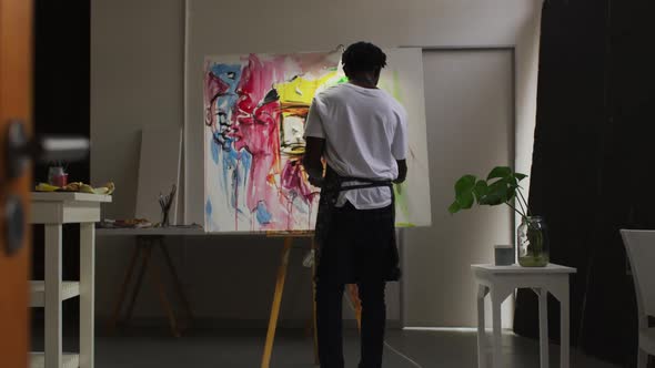 Rear view of african american male artist wearing apron painting on canvas at art studio