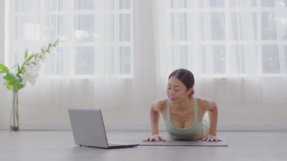 Wellness Attractive Asian woman practice yoga Cobra pose online course at home