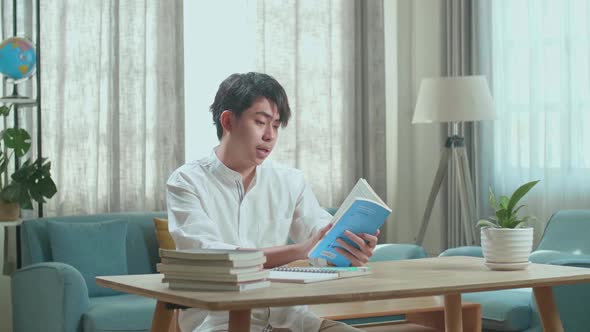 Asian Man Student Reading A Book While Studying At Home