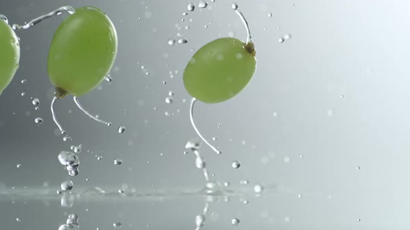 Green grapes falling and bouncing on water surface. Slow Motion.