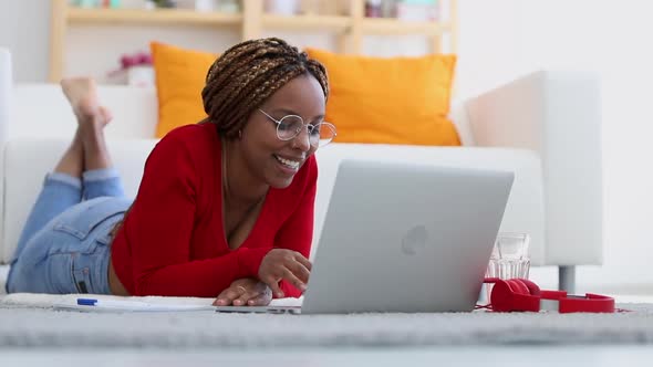 Beautiful African American Woman Talking and Lying on Floor with Laptop at Home Room Spbi