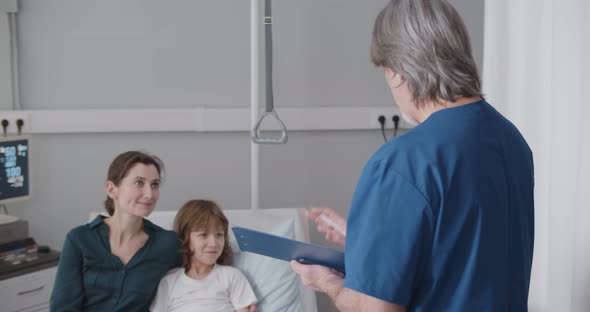 Aged Male Doctor Discussing Treatment with Kid Patient and Mother in Ward at Hospital