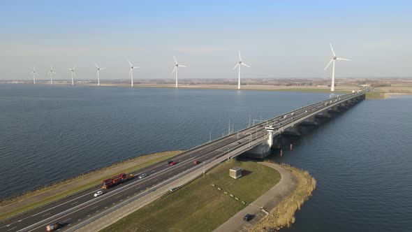 Aerial orbit over bascule bridge with traffic, wind turbines in distance, Netherlands