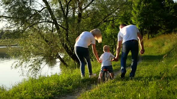 The Child Learns to Ride a Bike with His Parents in the Park