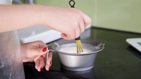 Closeup of Hairdresser's Hand Mixing Cream in Bowl in Salon