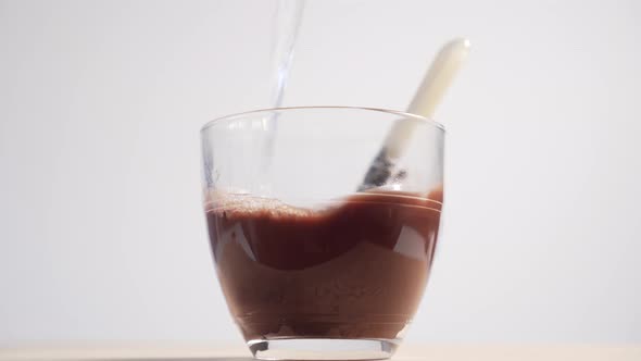 Boiling water fills a glass cup with cocoa powder 