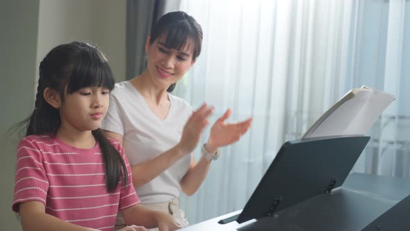 Asian happy mother teach young child daughter enjoy playing piano together in living room at home.