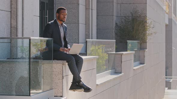 Thoughtful Mixed Race Businessman Black Man Millennial Wearing Suit Sitting Outdoors Typing on