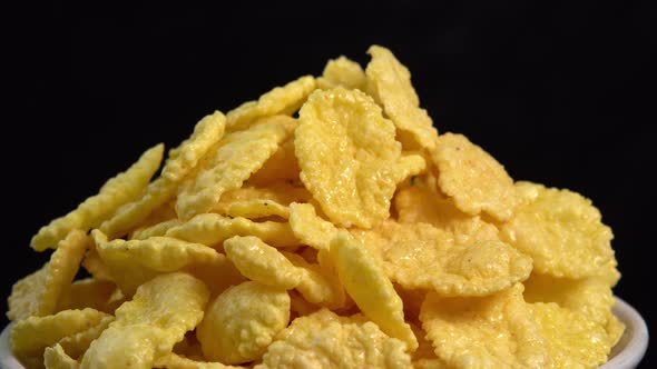 Crispy corn flakes rotating in bowl on black background close up, dry healthy breakfast