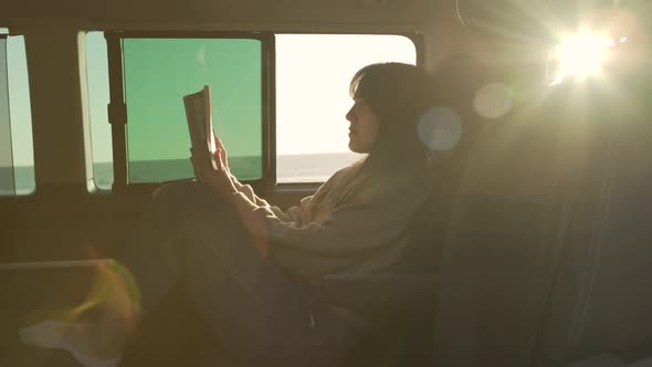 Traveling woman reading book in van at sunset