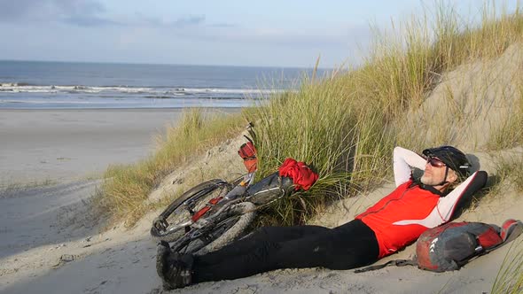 A man resting on the beach by his mountain bike.