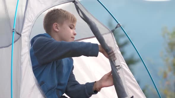 Hiker child boy resting in a tourist tent at mountain campsite.