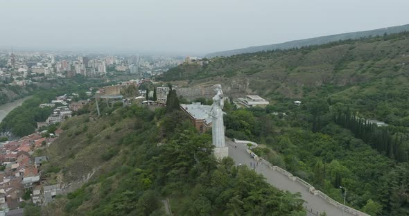 Arc aerial shot of the Kartlis Deda statue and the cityscape of Tbilisi.