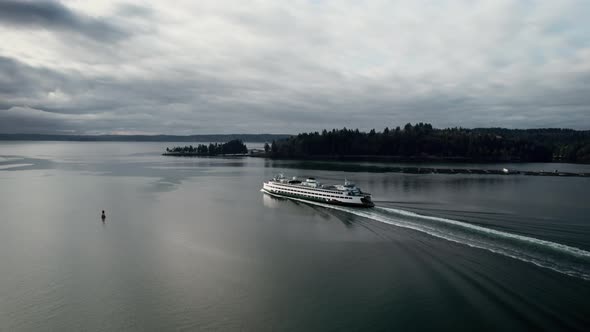 A Washington State ferry cruises out to open water, dark gloomy clouds reflect, aerial