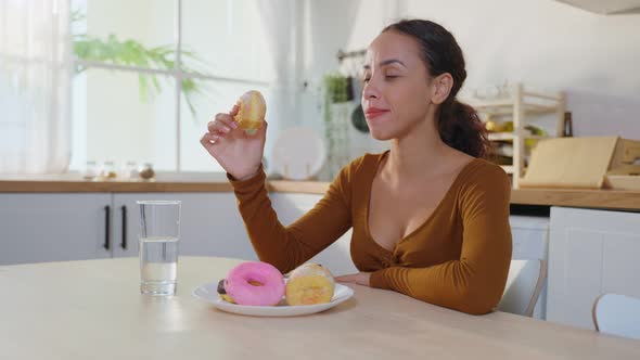 Latino attractive woman enjoy eat unhealthy foods bite sweet chocolate donut in kitchen at home.