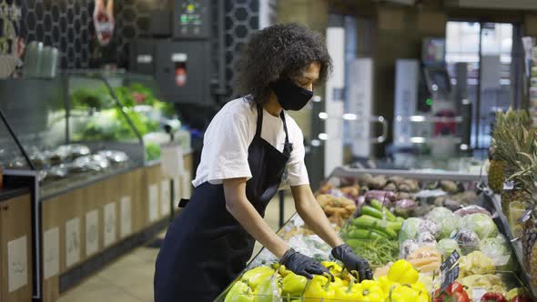 Mixed Race Grocery Store Employee in Face Mask and Gloves Putting Fresh Vegetables and Fruits